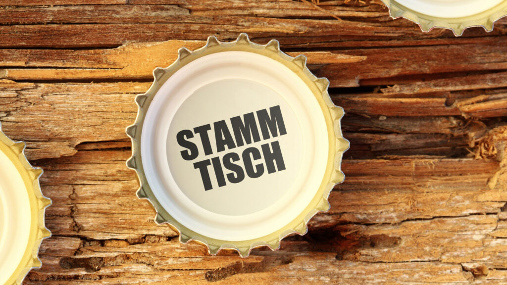 Kronkorken mit der Aufschrift „Stammtisch“ auf einem Holztisch